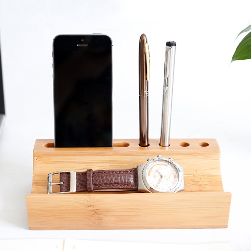 Front view of a bamboo desk organizer holding a smartphone, two pens, and a wristwatch — stylish workspace accessory for professionals.