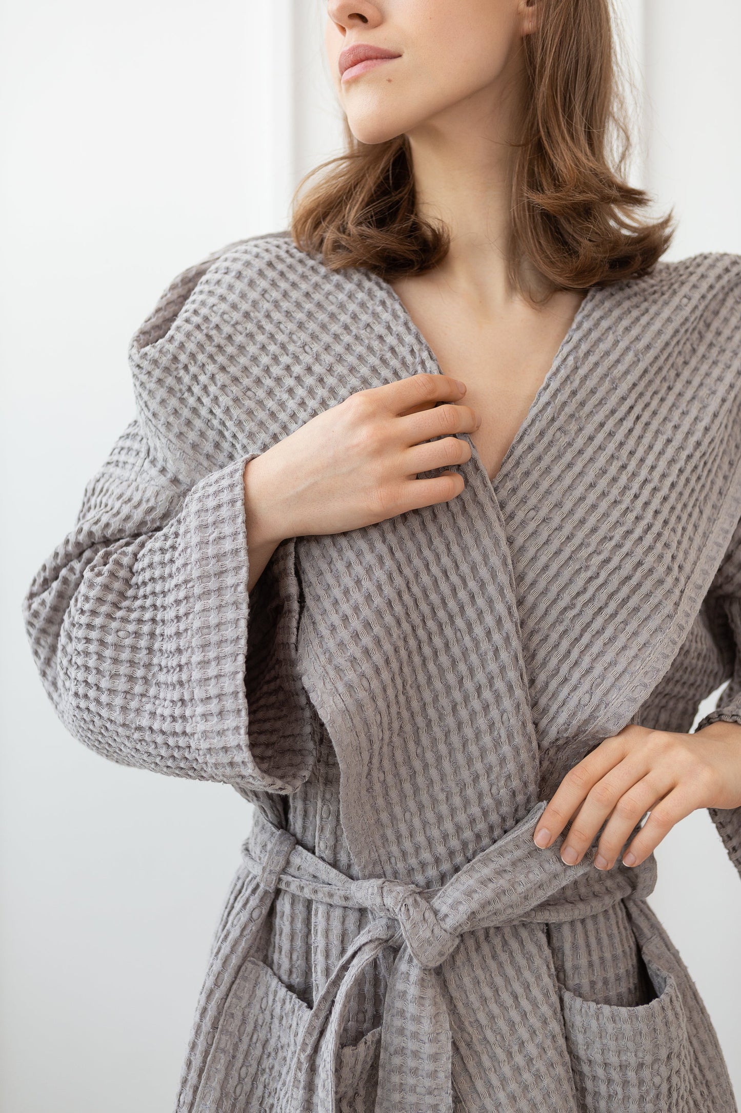 Detailed view of a woman wearing a grey waffle weave cotton bathrobe, showing texture, waist tie, and front pockets.