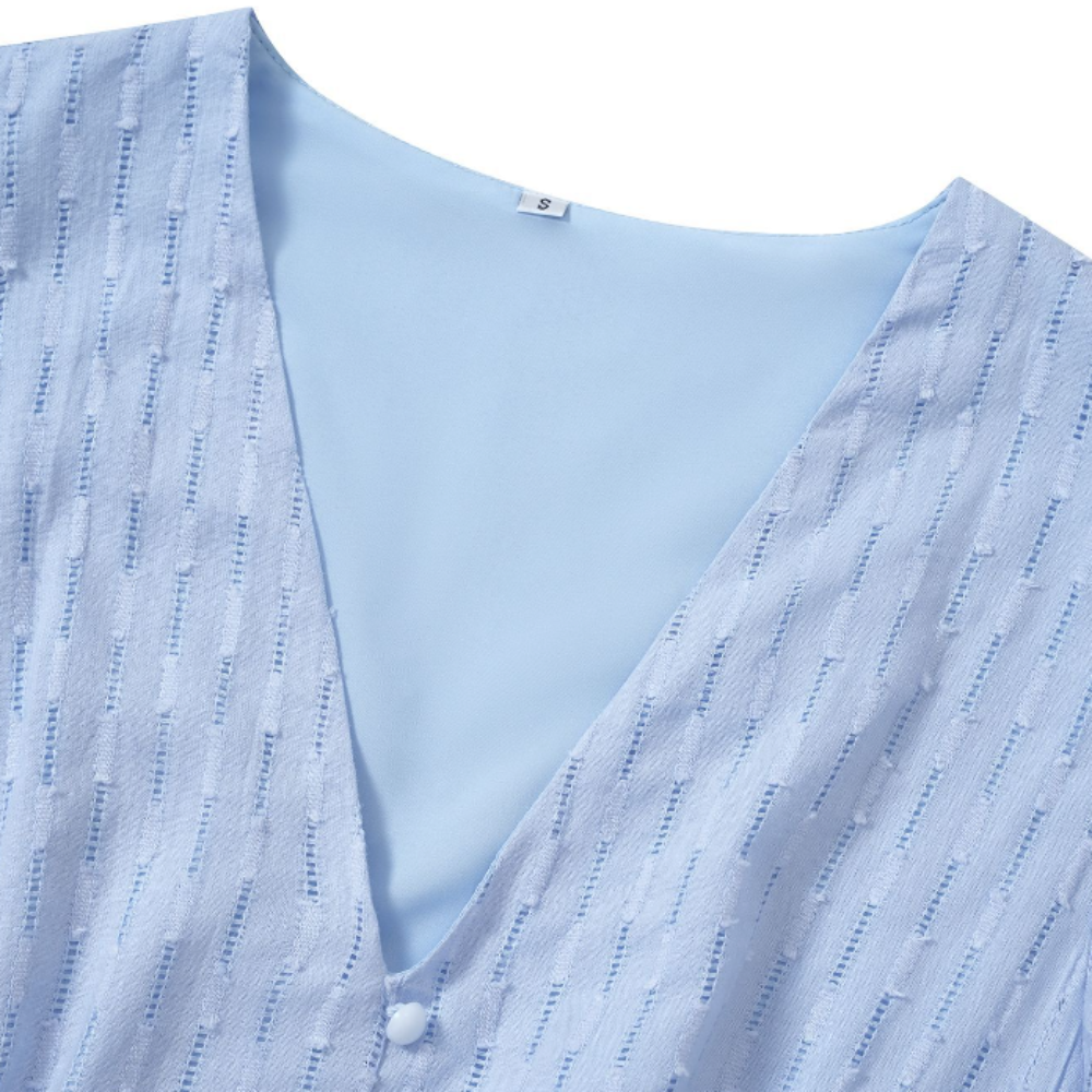 Detailed close-up of the light blue V-neck midi dress showing textured vertical pattern, soft lining, and front button fastening—highlighting the quality and craftsmanship of the fabric.