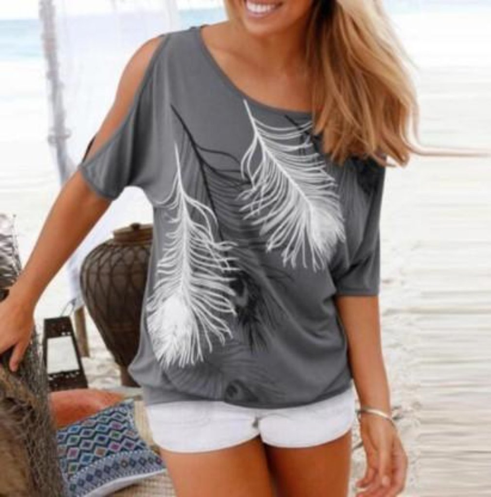 Smiling woman in a grey cold shoulder t-shirt with white feather print, styled with white shorts for a relaxed beach look.