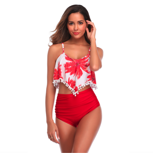 Woman walking in a red palm leaf print two-piece bikini featuring a flowy pom-pom trimmed top and high-waisted ruched bottoms.