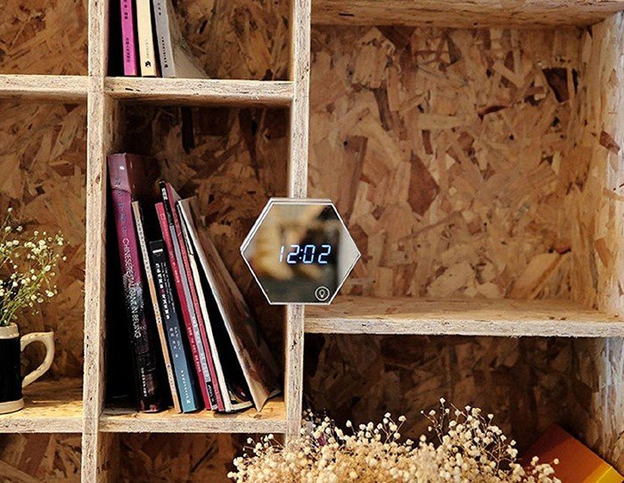 Hexagonal LED mirror clock displayed on a rustic wooden bookshelf with books and dried flowers, combining modern digital design with cosy home décor.