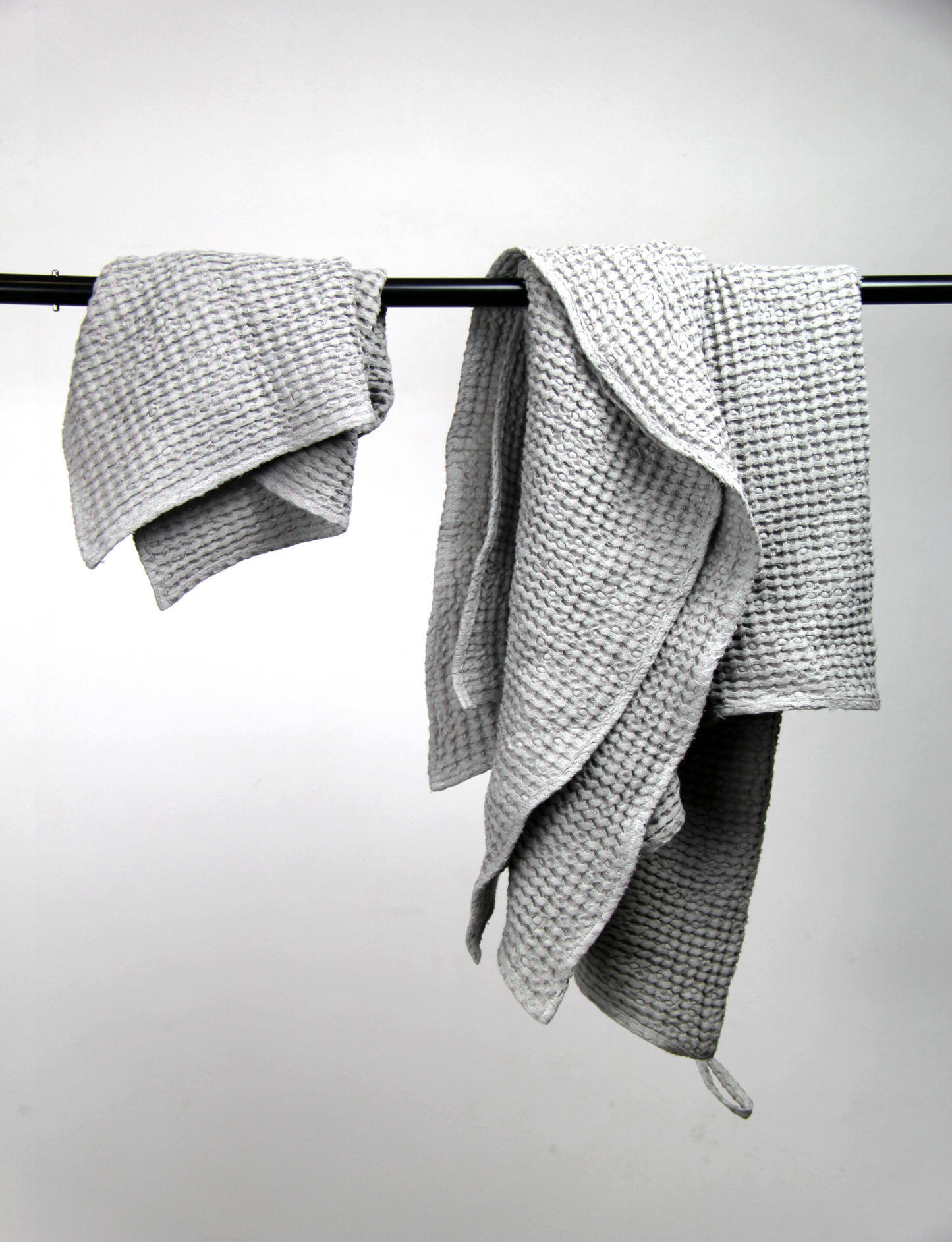 Light grey waffle-textured towels draped over a black metal bar against a white background