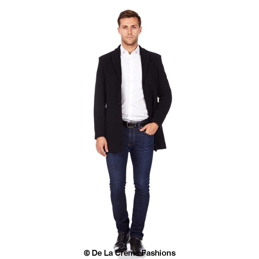 Man wearing a black slim-fit overcoat styled open over a white shirt, dark denim jeans, and black leather shoes—smart-casual layering from De La Creme Fashions for polished everyday wear.