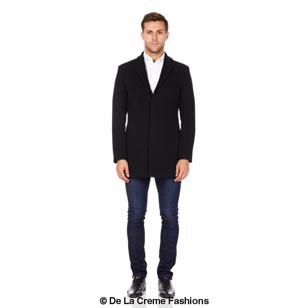 Man wearing a black slim-fit wool blend overcoat with a single-breasted design, styled with a white dress shirt, dark jeans, and black shoes—classic smart outerwear for versatile cold-weather style. © De La Creme Fashions