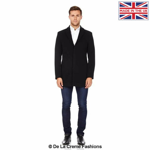 Man wearing a black slim-fit wool overcoat with a single-breasted front, styled with a white shirt and dark jeans. A British-made piece by De La Creme Fashions, highlighted with a “Made in the UK” badge.
