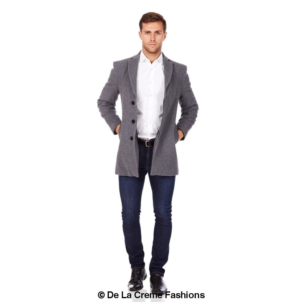 Man wearing a grey slim-fit wool overcoat with a double-button closure, styled open over a white shirt, navy jeans, and black dress shoes—timeless outerwear from De La Creme Fashions for a refined urban look.