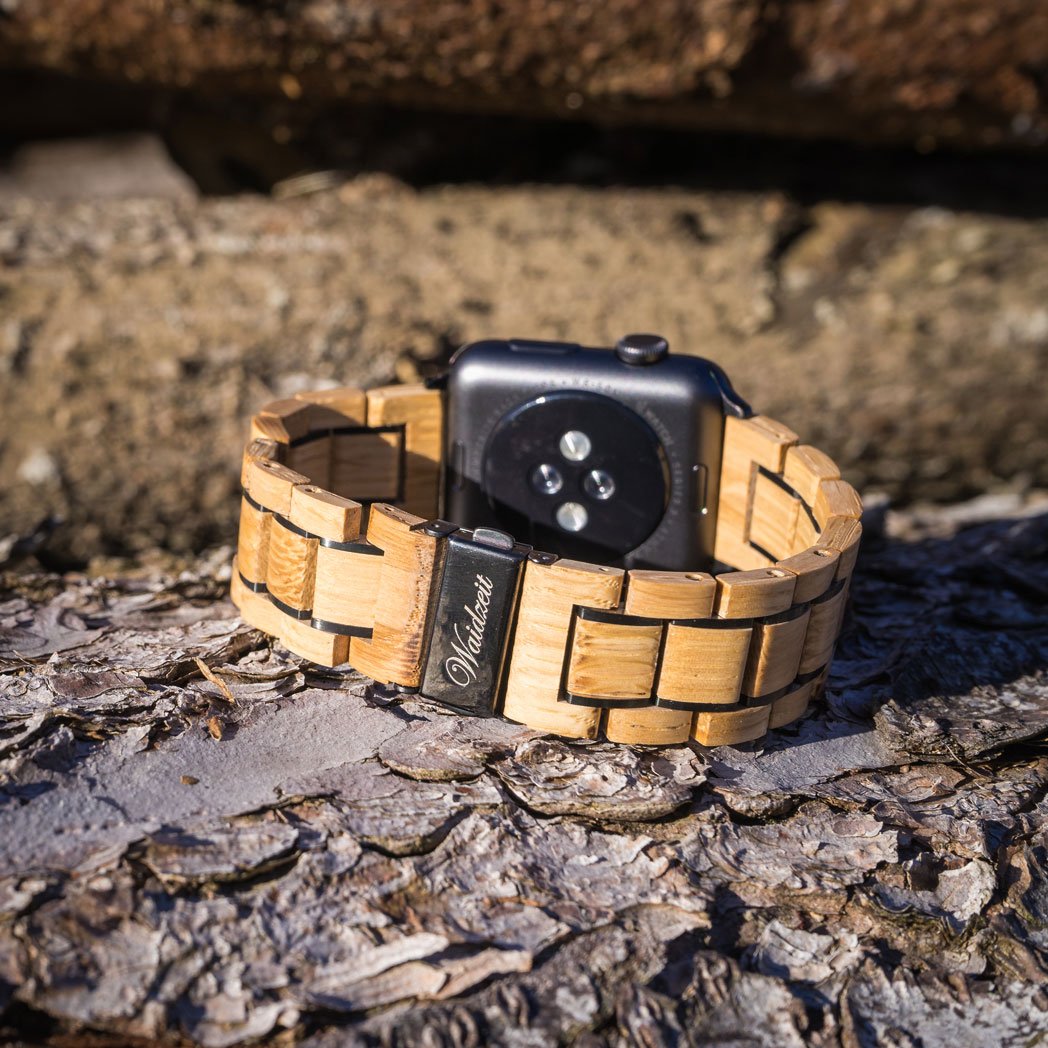 Close-up of Waidzeit Apple Watch strap made from sustainable oak wine barrel wood, showcasing engraved clasp detail on rustic bark background.