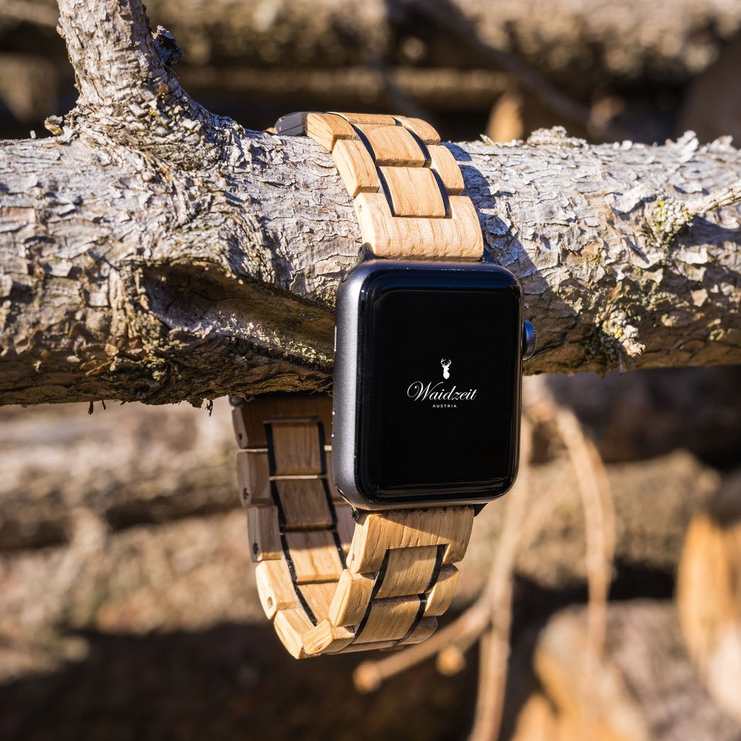Waidzeit Apple Watch strap crafted from upcycled oak wine barrel wood, elegantly draped over a natural tree branch in sunlight.