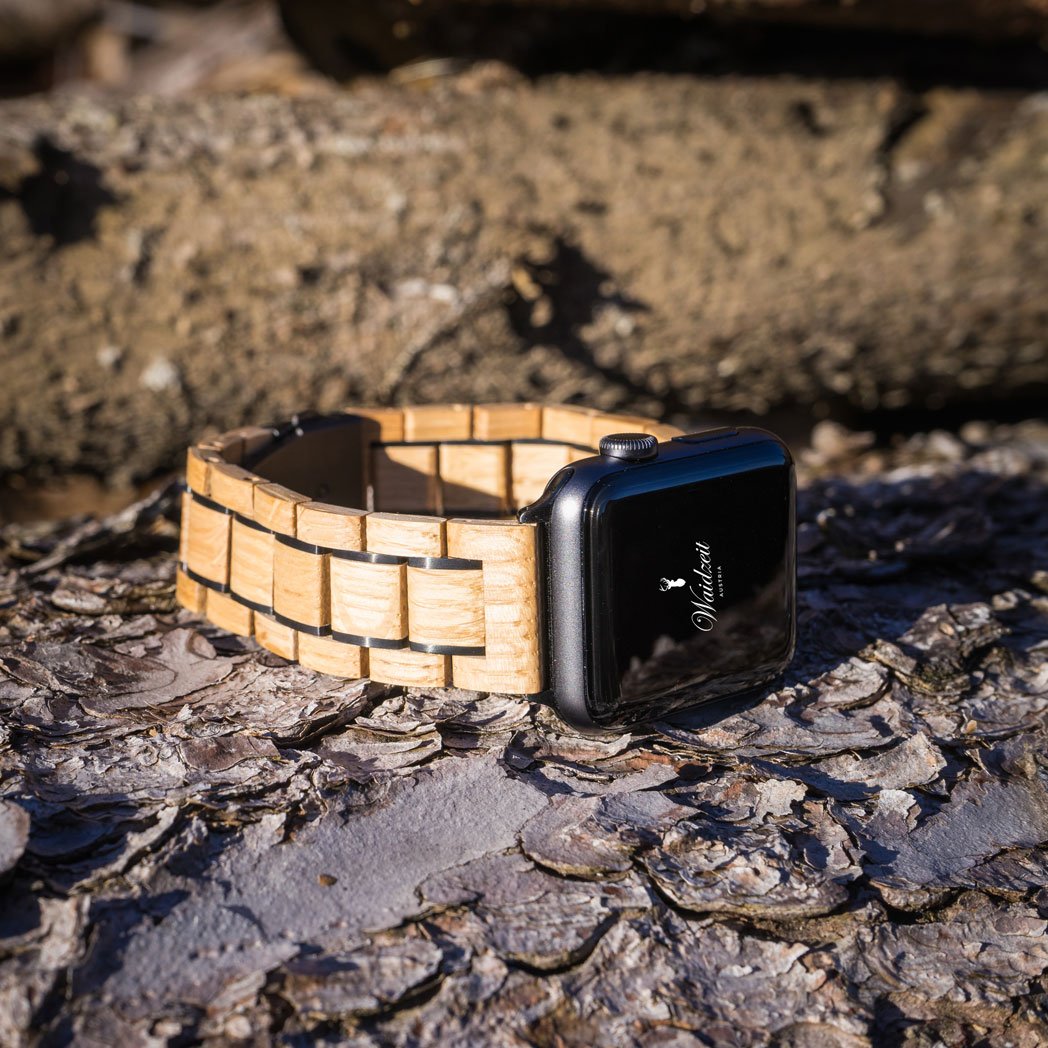 Waidzeit Apple Watch with handcrafted wooden strap made from reclaimed wine barrels, displayed on natural bark surface in outdoor lighting.