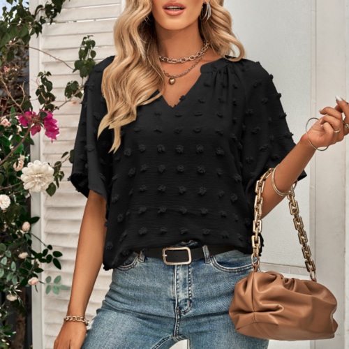 Woman wearing a black V-neck blouse with Swiss dot texture and flutter sleeves, paired with denim jeans and accessorized with a tan chain-handle handbag and layered necklaces.