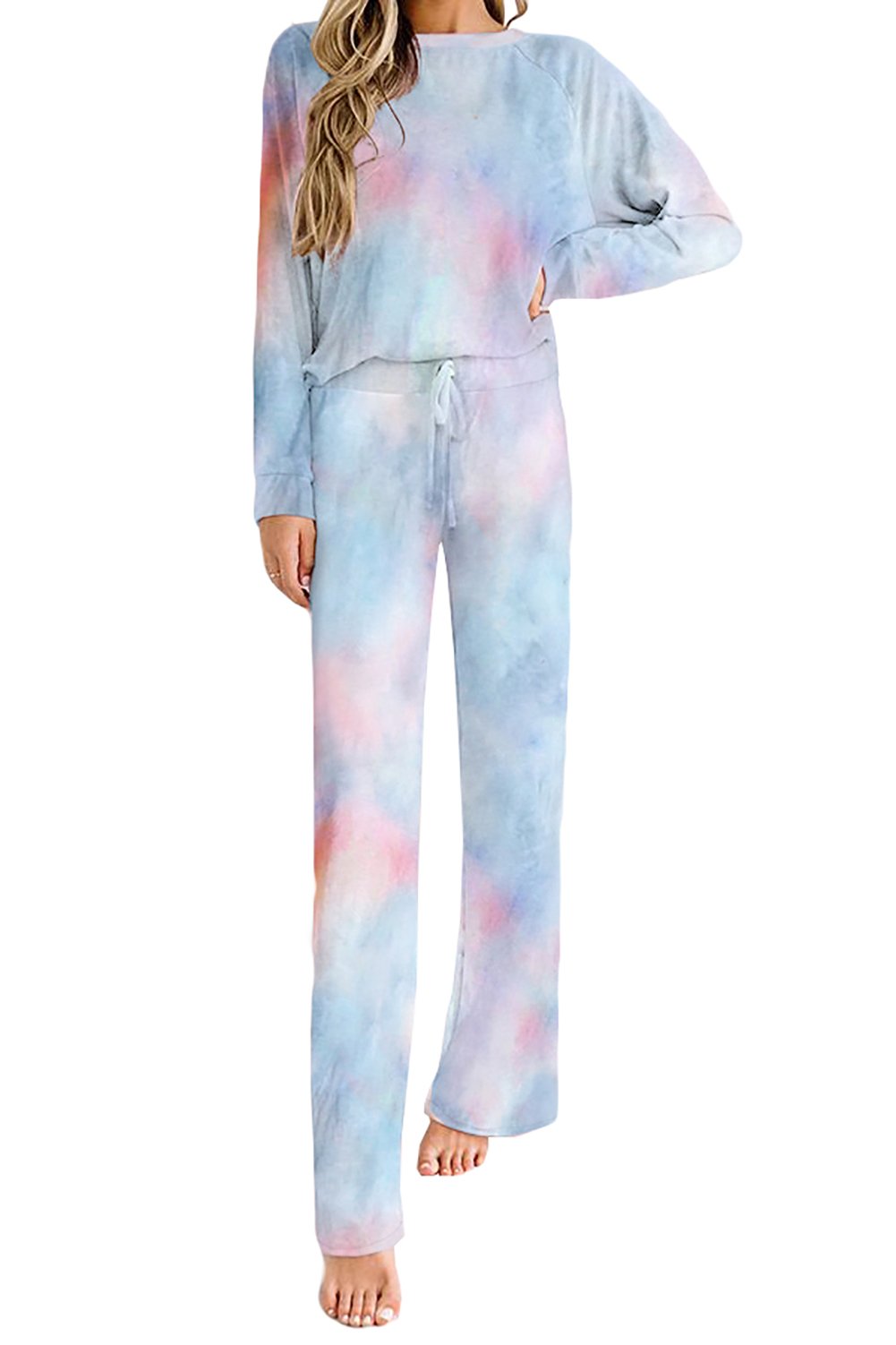 Woman wearing a pastel tie-dye loungewear set featuring a long-sleeve top and matching wide-leg drawstring pants in shades of blue, pink, and purple. She is barefoot and standing against a white background.
