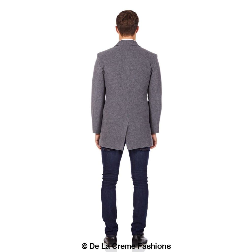 Rear view of a man wearing a grey slim-fit wool overcoat featuring structured shoulders and a center back vent, styled with dark jeans and black shoes—tailored design by De La Creme Fashions.