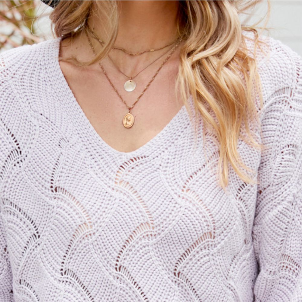 Detailed close-up of the lilac V-neck knit sweater highlighting its wave-textured open-stitch design and soft fabric, styled with layered gold necklaces for a delicate and feminine finish.