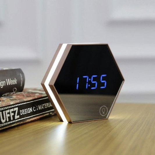 Modern hexagon-shaped LED desk clock with blue digital display and soft edge lighting, styled on a wooden surface beside design books — perfect for contemporary workspaces or minimalist interiors.
