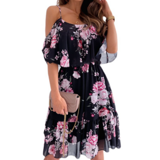 Woman wearing a navy blue cold-shoulder midi dress with pink floral print and ruffle overlay, styled with a beige clutch bag and gold accessories.