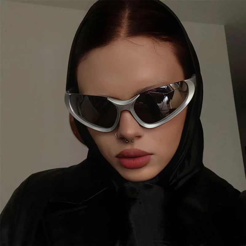 Person wearing reflective silver wraparound sunglasses and a black hooded outfit, showcasing a bold fashion look with a septum piercing and matte lipstick.
