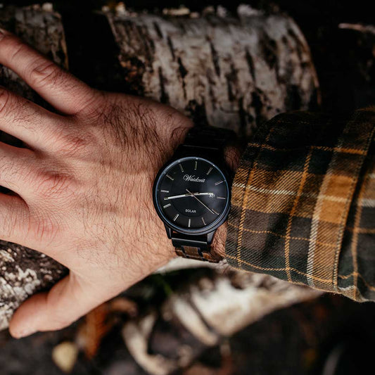 Waidzeit Mystic Solar men's watch with bog oak and stainless steel strap, worn on wrist against a rustic woodland background, showcasing the minimalist black dial with solar movement.