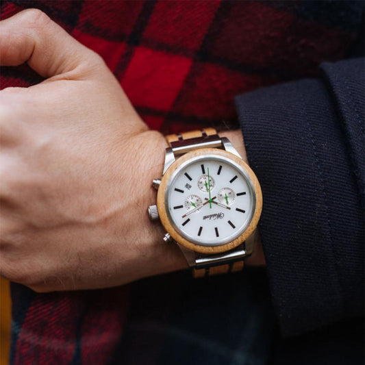 Close-up of a Waidzeit men's chronograph watch with a white dial, green hands, and wooden bezel, worn on a wrist against a red plaid background.