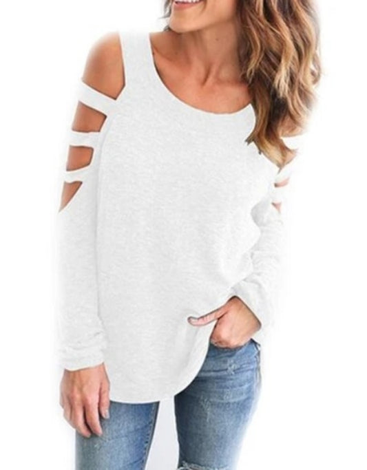 Woman wearing a white long sleeve top featuring cold shoulder cutouts and triple strap detailing on both arms, styled casually with blue jeans for a laid-back yet edgy everyday look.