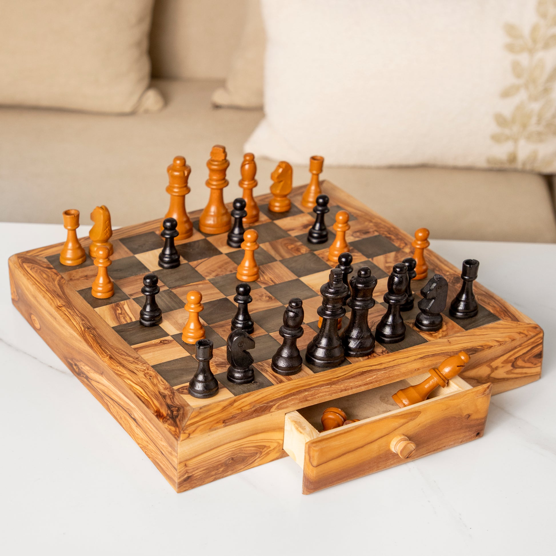 Luxury wooden chess set with natural and dark pieces, displayed on a square inlaid board with an open storage drawer, placed on a white marble surface.